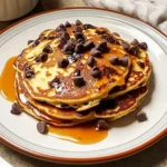 Fluffy chocolate chip pancakes stacked high with melted chocolate and a pat of butter on top