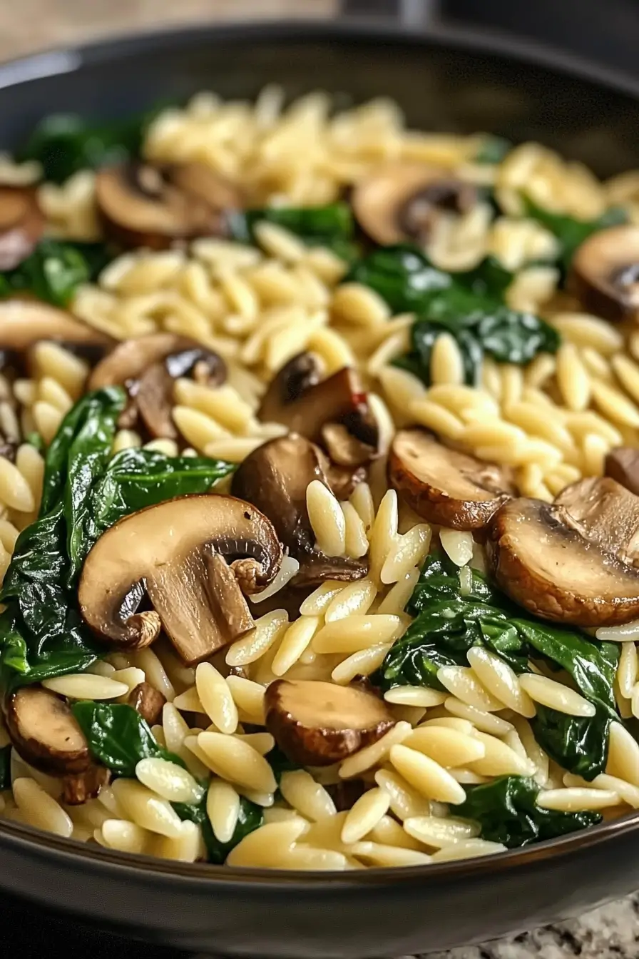 Creamy Spinach Mushroom Orzo in a skillet garnished with fresh herbs and Parmesan cheese
